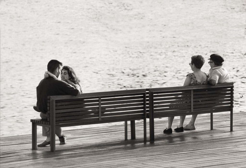 Dos parejas en los extremos de un banco frente al mar simbolizan el amor con el paso del tiempo