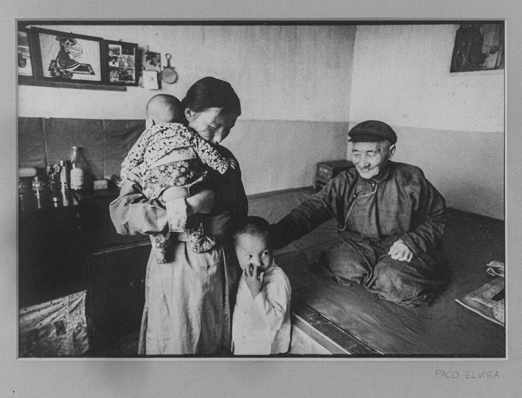 Interior de un hogar chino donde una madre está con sus dos hijos y en la mesa está el abuelo. 