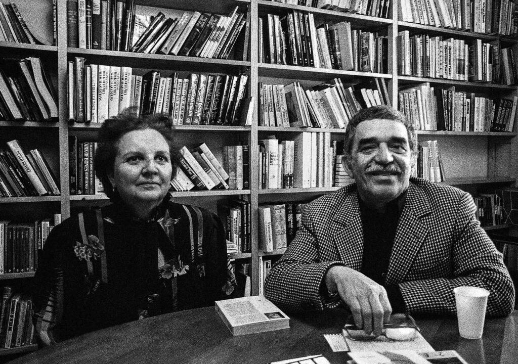 Carmen y Gabo sentado en la mesa de la sala de reuniones del despacho de la agente literaria y rodeados de libros. 